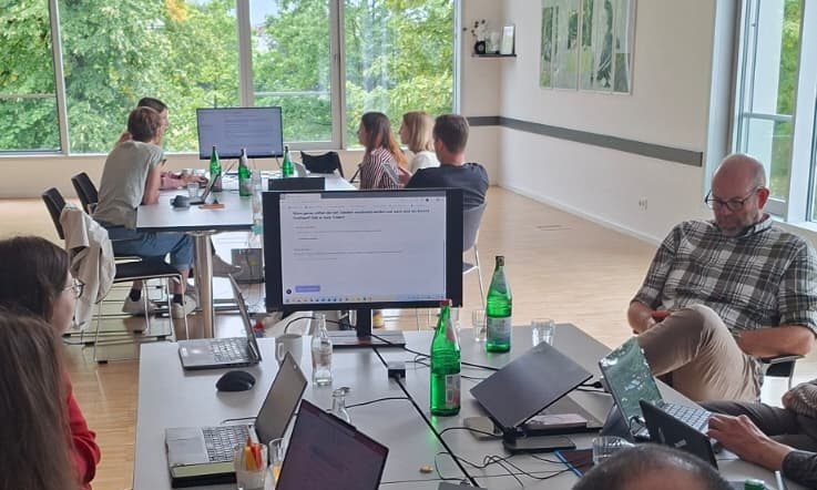 Teilnehmende des Hackathons an langen Tischreihen mit Laptops