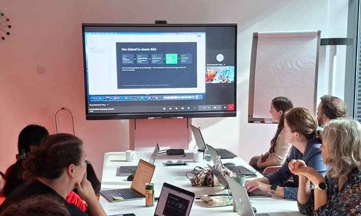 Teilnehmende des Bootcamps arbeiten an Laptops, vorne ein Bildschirm mit dem Ablauf