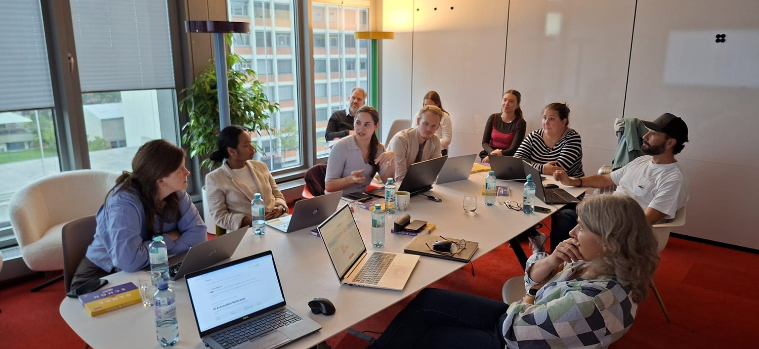 Gruppe am Konferenztisch mit Laptops, eine Teilnehmerin erklärt gerade etwas
